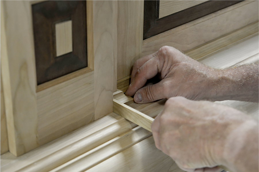 A cabinet maker is hand-crafting the molding details on a custom wood hood at the manufacturing facility.